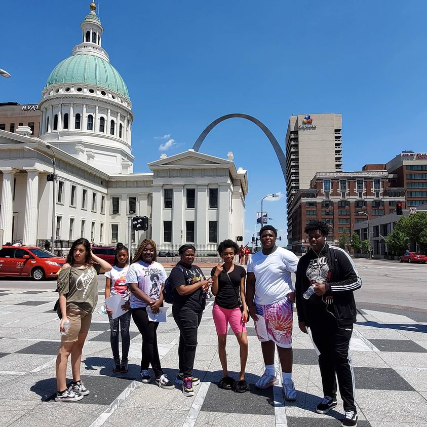 A group of Kulture students stand in downtown St. Louis in front of the capitol building, with the arch in the distance. 